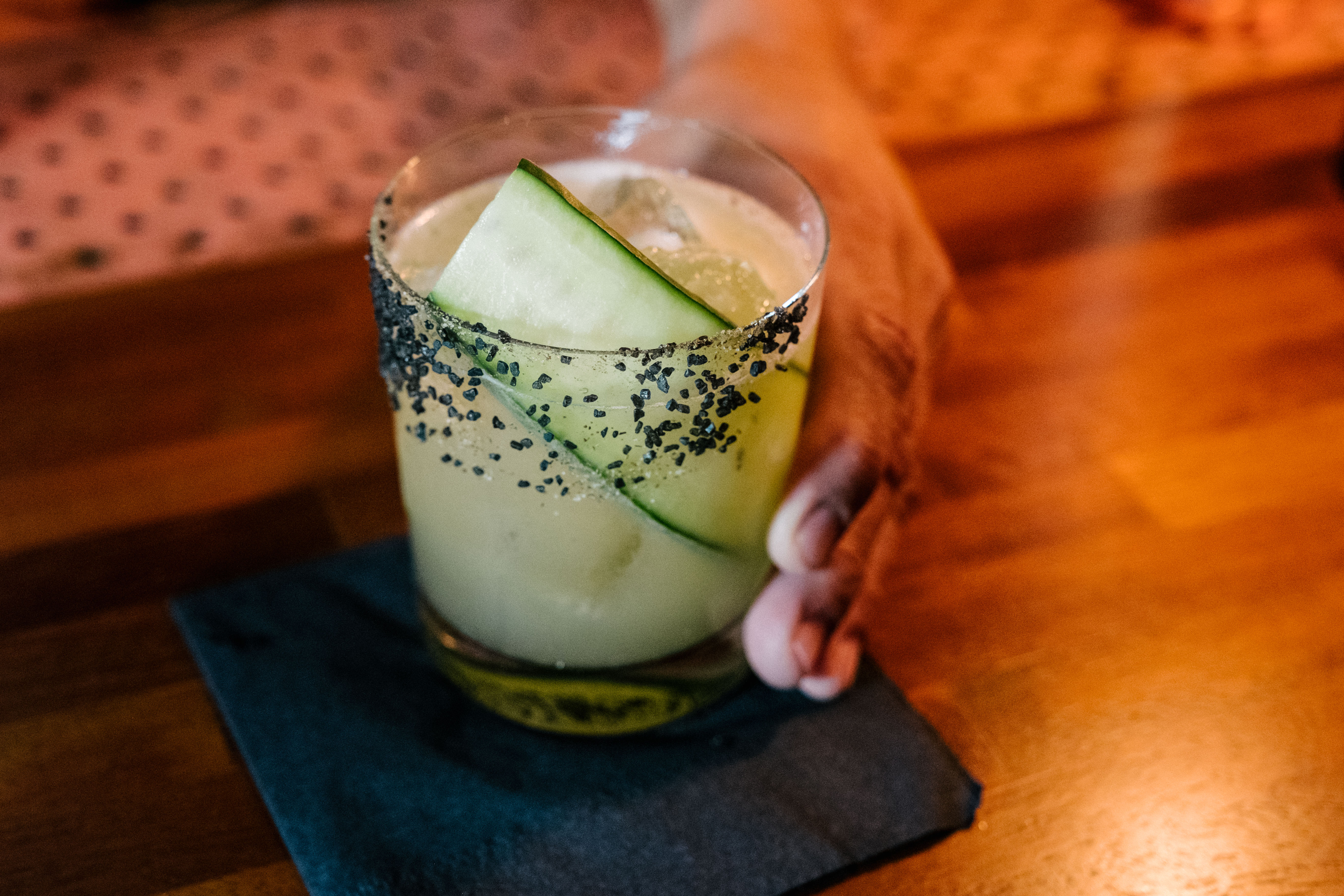 Hand holding cocktail with cucumber